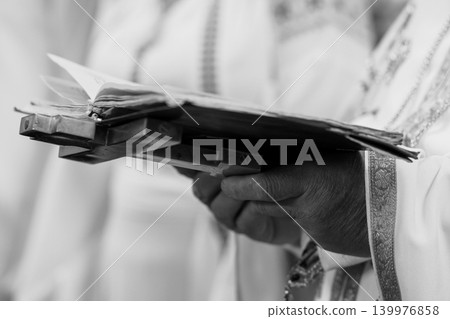 Priest Holding Open Religious Book During Christian Liturgy in Black and White Cinematic Style Priest Holding Open Religious Book During Christian Liturgy in Black and White Cinematic Style 139976858