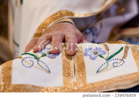 Close up of Priest Hand Touching Embroidered White and Gold Religious Vestment with Floral Pattern 139976859