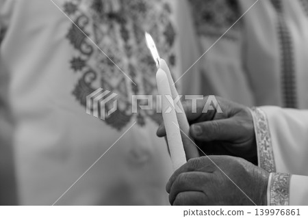 Person Holding Lit White Candle in Traditional Embroidered Religious Clothing Black and White Person Holding Lit White Candle in Traditional Embroidered Religious Clothing Black and White 139976861