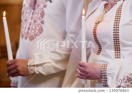 Couple in Traditional White Embroidered Folk Costumes Holding Lit Taper Candles at Ceremony Couple in Traditional White Embroidered Folk Costumes Holding Lit Taper Candles at Ceremony 139976863