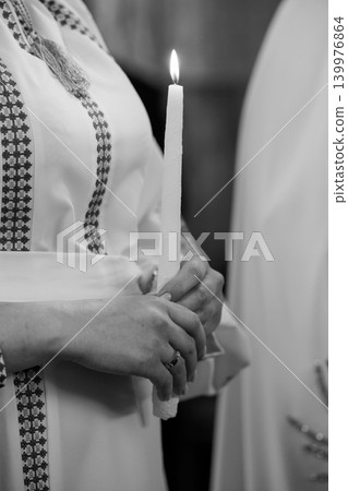 Close up of hands holding a burning white candle in traditional ethnic clothing, black and white photography 139976864