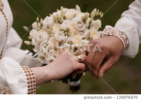 Bride and Groom Holding Hands with White Rose Bouquet and Gold Wedding Rings in Traditional Embroidery Bride and Groom Holding Hands with White Rose Bouquet and Gold Wedding Rings in Traditional Embroidery 139976870