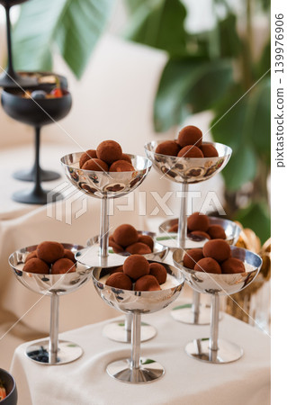 Chocolate Truffles Served in Elegant Silver Martini Glasses on White Cloth with Green Foliage Chocolate Truffles Served in Elegant Silver Martini Glasses on White Cloth with Green Foliage 139976906