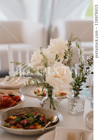 Elegant White Roses in Glass Vase with Gourmet Salad and Appetizers on White Table 139976915