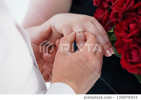 Close up of Man Placing Diamond Engagement Ring on Woman Hand with Red Roses Close up of Man Placing Diamond Engagement Ring on Woman Hand with Red Roses 139976933