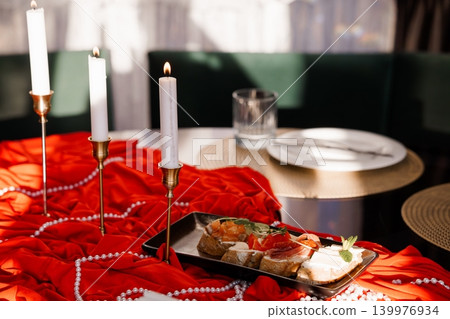 Elegant Table Setting with Red Velvet Fabric, White Taper Candles, and Appetizer Platter for Romantic Dinner Elegant Table Setting with Red Velvet Fabric, White Taper Candles, and Appetizer Platter for Romantic Dinner 139976934