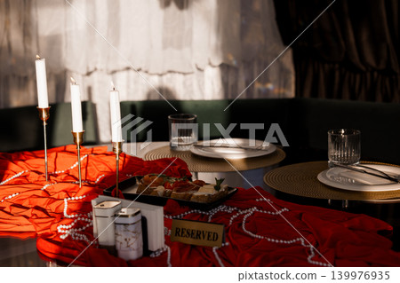 Elegant Restaurant Table Setting with Red Fabric, White Candles, and Reserved Sign for Romantic Dinner Elegant Restaurant Table Setting with Red Fabric, White Candles, and Reserved Sign for Romantic Dinner 139976935