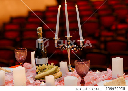 Elegant Dinner Setting with Candelabra, Champagne, and Fruit on Red Velvet Theater Seating Background Elegant Dinner Setting with Candelabra, Champagne, and Fruit on Red Velvet Theater Seating Background 139976956