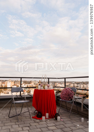 Romantic Dinner for Two with Red Tablecloth and Roses on Rooftop Terrace overlooking City Skyline 139976987