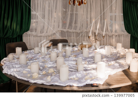 Elegant Round Dining Table with White Silk Cloth and Many White Pillar Candles for Romantic Wedding Decor Elegant Round Dining Table with White Silk Cloth and Many White Pillar Candles for Romantic Wedding Decor 139977005