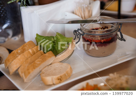 Appetizer Platter with Pate in Glass Jar, Toasted Bread Slices, and Fresh Green Lettuce on White Plate 139977020