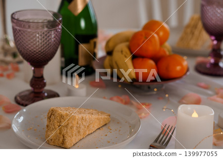 Slice of Sponge Cake on White Plate with Fruit Bowl and Glassware on Table with Candles Slice of Sponge Cake on White Plate with Fruit Bowl and Glassware on Table with Candles 139977055