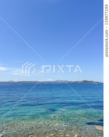 Captivating image of a serene blue sea with clear waters and distant mountains under a vast sky. Ideal for travel, nature, and landscape themes, evoking tranquility and peace 139977289