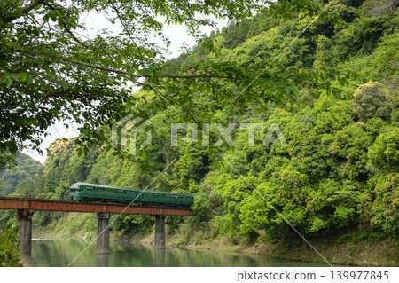 The fresh green Yufuin train crosses a railway bridge surrounded by lush greenery. The fresh green Yufuin train crosses a railway bridge surrounded by lush greenery. 139977845