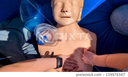 A professional paramedic teacher is teaching a boy first aid and CPR training for kids using a medical mannequin. This outdoor workshop focuses on practicing chest compressions 139978387