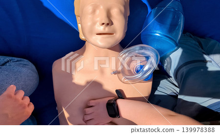 A professional paramedic teacher is teaching a boy first aid and CPR training for kids using a medical mannequin. This outdoor workshop focuses on practicing chest compressions A professional paramedic teacher is teaching a boy first aid and CPR training for kids using a medical mannequin. This outdoor workshop focuses on practicing chest compressions 139978388