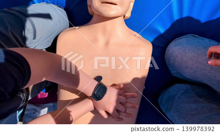 A professional paramedic teacher is teaching a boy first aid and CPR training for kids using a medical mannequin. This outdoor workshop focuses on practicing chest compressions A professional paramedic teacher is teaching a boy first aid and CPR training for kids using a medical mannequin. This outdoor workshop focuses on practicing chest compressions 139978392