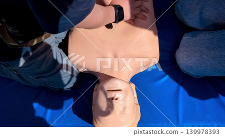 A professional paramedic teacher is teaching a boy first aid and CPR training for kids using a medical mannequin. This outdoor workshop focuses on practicing chest compressions 139978393