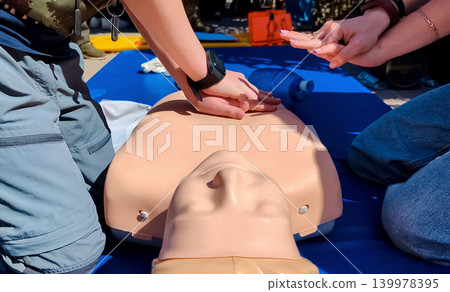 A professional paramedic teacher is teaching a boy first aid and CPR training for kids using a medical mannequin. This outdoor workshop focuses on practicing chest compressions A professional paramedic teacher is teaching a boy first aid and CPR training for kids using a medical mannequin. This outdoor workshop focuses on practicing chest compressions 139978395