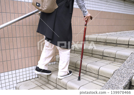 An elderly woman with a cane climbs the stairs in Yokohama, Japan, taking breaks along the city's urban landscape. An aging society. Even these gentle stairs become difficult for the elderly. An elderly woman with a cane climbs the stairs in Yokohama, Japan, taking breaks along the city's urban landscape. An aging society. Even these gentle stairs become difficult for the elderly. 139978466