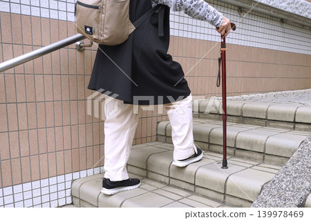 An elderly woman with a cane climbs the stairs in Yokohama, Japan, taking breaks along the city's urban landscape. An aging society. Even these gentle stairs become difficult for the elderly. An elderly woman with a cane climbs the stairs in Yokohama, Japan, taking breaks along the city's urban landscape. An aging society. Even these gentle stairs become difficult for the elderly. 139978469