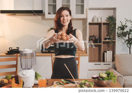 Woman preparing green smoothie in bright kitchen with fresh fruits and vegetables, healthy eating lifestyle moment in natural daylight 139978622