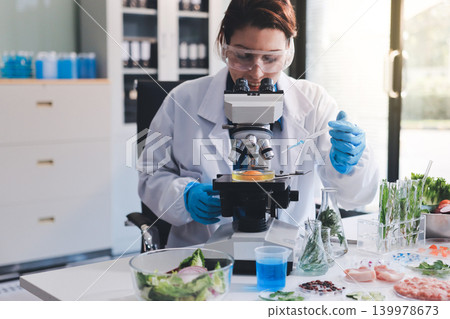 Scientists in lab coats work with plants in a modern lab, focusing on research and experimentation under bright, sterile conditions. Scientists in lab coats work with plants in a modern lab, focusing on research and experimentation under bright, sterile conditions. 139978673
