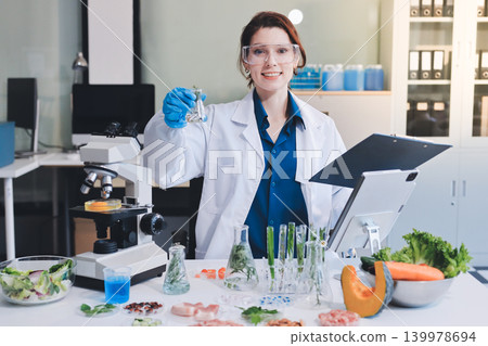 Scientists in lab coats work with plants in a modern lab, focusing on research and experimentation under bright, sterile conditions. 139978694