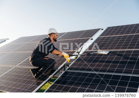 High up, cleaning the surface with a mop. Male solar engineer examining photovoltaic panels at a power station High up, cleaning the surface with a mop. Male solar engineer examining photovoltaic panels at a power station 139978760