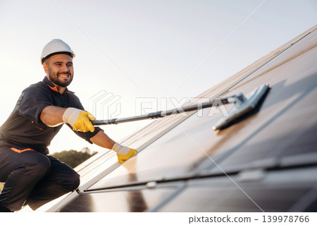 Mopping the surface. Male solar engineer examining photovoltaic panels at a power station Mopping the surface. Male solar engineer examining photovoltaic panels at a power station 139978766