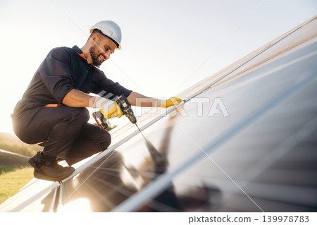 Installation, using the drill. Male solar engineer examining photovoltaic panels at a power station Installation, using the drill. Male solar engineer examining photovoltaic panels at a power station 139978783