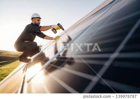 Installation, using the drill. Male solar engineer examining photovoltaic panels at a power station 139978787