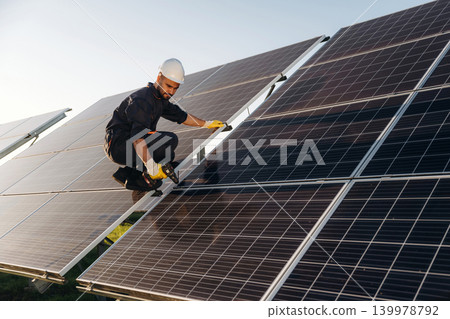 Service, sitting with drill and doing installation. Male solar engineer examining photovoltaic panels at a power station Service, sitting with drill and doing installation. Male solar engineer examining photovoltaic panels at a power station 139978792