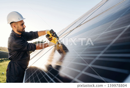 Yellow drill is in hands, installation process. Male solar engineer examining photovoltaic panels at a power station Yellow drill is in hands, installation process. Male solar engineer examining photovoltaic panels at a power station 139978804