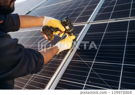 At daytime, installation, using drill. Male solar engineer examining photovoltaic panels at a power station At daytime, installation, using drill. Male solar engineer examining photovoltaic panels at a power station 139978808