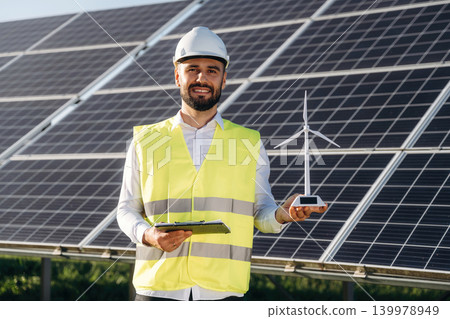 Small windmill model. Male solar engineer examining photovoltaic panels at a power station Small windmill model. Male solar engineer examining photovoltaic panels at a power station 139978949