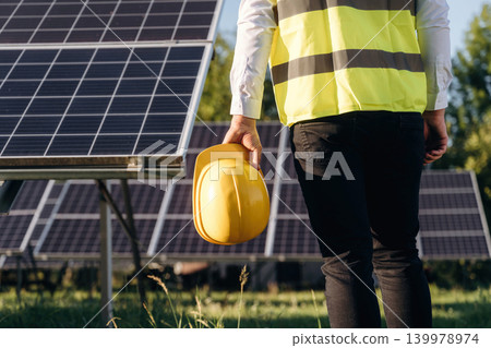 In yellow colored professional uniform. Male solar engineer examining photovoltaic panels at a power station In yellow colored professional uniform. Male solar engineer examining photovoltaic panels at a power station 139978974