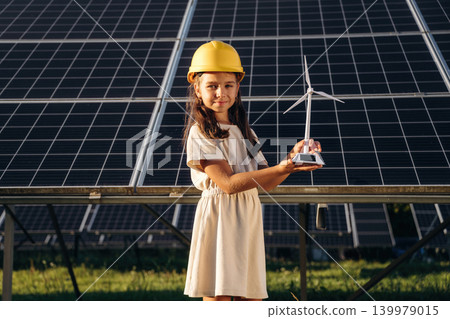 Holding little model of windmill. Happy girl is near renewable energy equipment under bright sunlight Holding little model of windmill. Happy girl is near renewable energy equipment under bright sunlight 139979015
