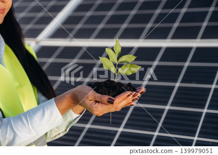 Fresh plant sprout holding in hands. Female solar engineer inspecting photovoltaic panels during outdoor maintenance work Fresh plant sprout holding in hands. Female solar engineer inspecting photovoltaic panels during outdoor maintenance work 139979051