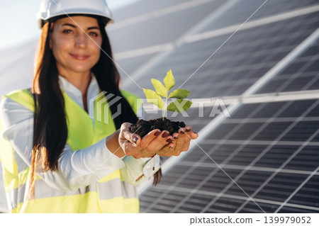 Fresh plant sprout holding in hands. Female solar engineer inspecting photovoltaic panels during outdoor maintenance work 139979052