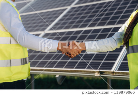Handshake, cooperation, success. Two solar engineers standing together at a photovoltaic field, in bright safety vests Handshake, cooperation, success. Two solar engineers standing together at a photovoltaic field, in bright safety vests 139979060