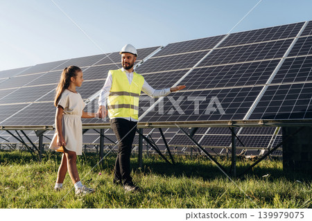 Friendly engineer showing renewable-energy equipment to a young visitor outdoors Friendly engineer showing renewable-energy equipment to a young visitor outdoors 139979075