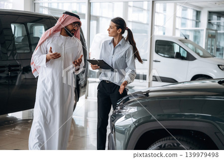 Active conversation, sharing information. Middle eastern client discussing car purchase in modern dealership Active conversation, sharing information. Middle eastern client discussing car purchase in modern dealership 139979498
