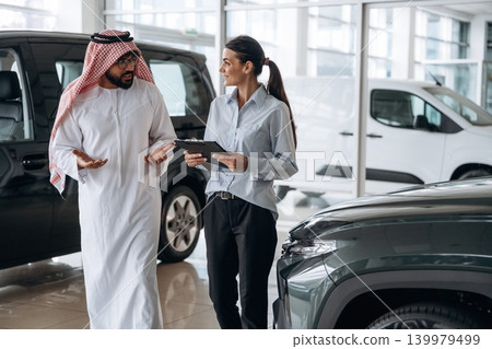 Active conversation, sharing information. Middle eastern client discussing car purchase in modern dealership Active conversation, sharing information. Middle eastern client discussing car purchase in modern dealership 139979499