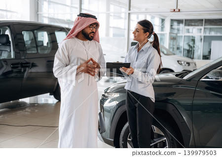 At daytime, showing information from notepad. Middle eastern client discussing car purchase in modern dealership At daytime, showing information from notepad. Middle eastern client discussing car purchase in modern dealership 139979503