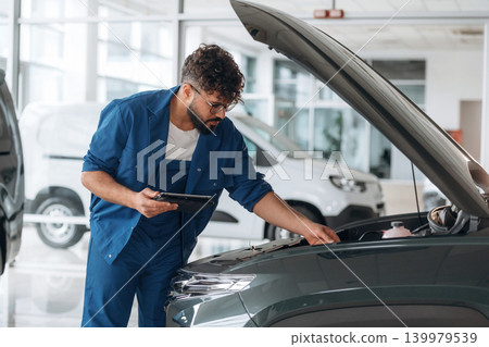 Hood is opened. Auto service specialist examining vehicle condition Hood is opened. Auto service specialist examining vehicle condition 139979539