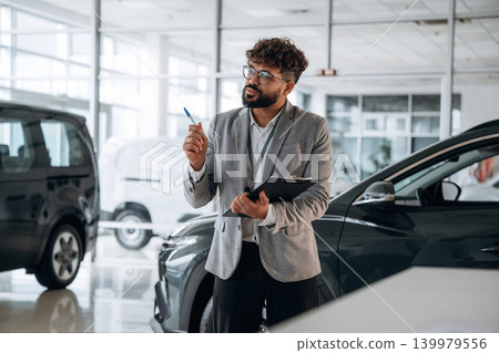 Standing, front view. Confident car salesman using digital tablet inside modern showroom 139979556