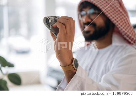 Arab businessman holding cash inside modern car showroom Arab businessman holding cash inside modern car showroom 139979563