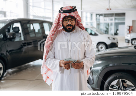 Arab businessman holding cash inside modern car showroom 139979564