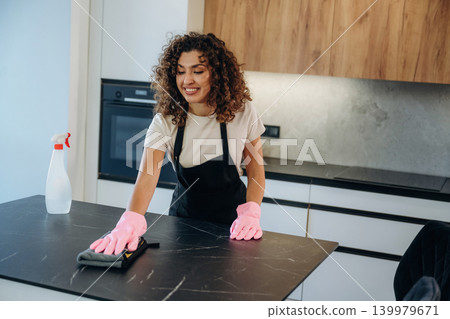 Spray and cloth. White woman cleaning the kitchen wearing pink gloves Spray and cloth. White woman cleaning the kitchen wearing pink gloves 139979671